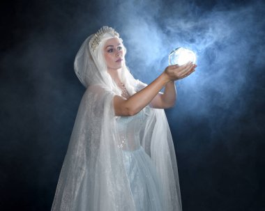 portrait beautiful blonde fantasy maiden faery wearing medieval fairytale ballgown costume, white cape and crystal crown. holding glowing crystal ball orb  isolated dark studio background with mystical smoke fog backlight lighting effect clipart