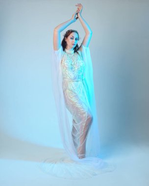 Beyaz inci bir elbise giyen kızıl saçlı bir deniz kızının fantezi stüdyosu portresi, peri masalı kostümü. Akan kumaş ve ruhani stüdyo ışıklarıyla klasik bir duruş sergilediler.