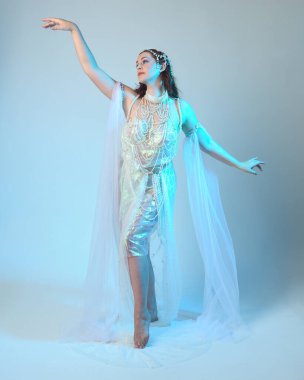 Beyaz inci bir elbise giyen kızıl saçlı bir deniz kızının fantezi stüdyosu portresi, peri masalı kostümü. Akan kumaş ve ruhani stüdyo ışıklarıyla klasik bir duruş sergilediler.