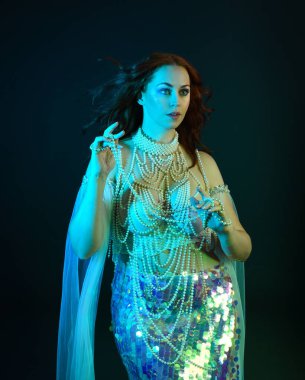 Fantezi stüdyo portresi, beyaz inci elbise giyen kızıl saçlı bir deniz kızı peri modeli, peri masalı kostümü. Akan kumaşlı, ruhsal kasvetli stüdyo ışıklandırmalı klasik poz.