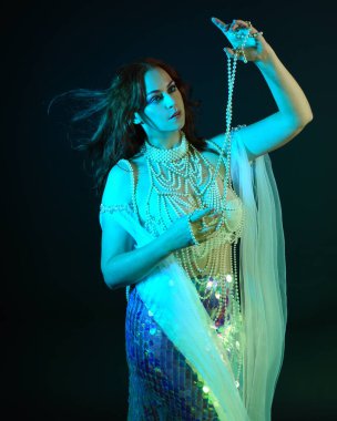 Fantezi stüdyo portresi, beyaz inci elbise giyen kızıl saçlı bir deniz kızı peri modeli, peri masalı kostümü. Akan kumaşlı, ruhsal kasvetli stüdyo ışıklandırmalı klasik poz.