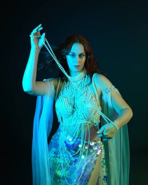 Fantezi stüdyo portresi, beyaz inci elbise giyen kızıl saçlı bir deniz kızı peri modeli, peri masalı kostümü. Akan kumaşlı, ruhsal kasvetli stüdyo ışıklandırmalı klasik poz.