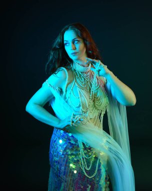 Fantezi stüdyo portresi, beyaz inci elbise giyen kızıl saçlı bir deniz kızı peri modeli, peri masalı kostümü. Akan kumaşlı, ruhsal kasvetli stüdyo ışıklandırmalı klasik poz.