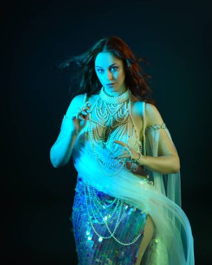 Fantezi stüdyo portresi, beyaz inci elbise giyen kızıl saçlı bir deniz kızı peri modeli, peri masalı kostümü. Akan kumaşlı, ruhsal kasvetli stüdyo ışıklandırmalı klasik poz.