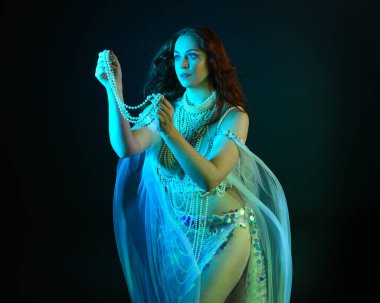 Fantezi stüdyo portresi, beyaz inci elbise giyen kızıl saçlı bir deniz kızı peri modeli, peri masalı kostümü. Akan kumaşlı, ruhsal kasvetli stüdyo ışıklandırmalı klasik poz.