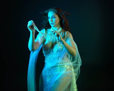 Fantezi stüdyo portresi, beyaz inci elbise giyen kızıl saçlı bir deniz kızı peri modeli, peri masalı kostümü. Akan kumaşlı, ruhsal kasvetli stüdyo ışıklandırmalı klasik poz.