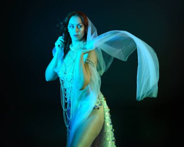 Fantezi stüdyo portresi, beyaz inci elbise giyen kızıl saçlı bir deniz kızı peri modeli, peri masalı kostümü. Akan kumaşlı, ruhsal kasvetli stüdyo ışıklandırmalı klasik poz.