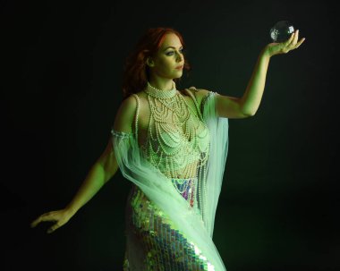 Fantezi stüdyo portresi, beyaz inci elbise giyen kızıl saçlı bir deniz kızı peri modeli, peri masalı kostümü. Akan kumaşlı, ruhsal kasvetli stüdyo ışıklandırmalı klasik poz.