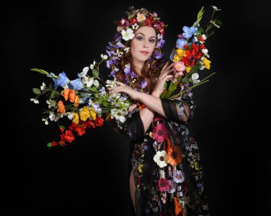 Celtic Bahar Tanrıçası Fantezi Kostümü Olarak Bir Kadın Modelinin Stüdyosu Gerçek Çiçekler ve başlıklı Beltane Pagan Mitolojisinden esinlenilerek izole edilmiş Karanlık Stüdyo Arkaplanı üzerine poz vermektedir.