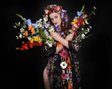 Celtic Bahar Tanrıçası Fantezi Kostümü Olarak Bir Kadın Modelinin Stüdyosu Gerçek Çiçekler ve başlıklı Beltane Pagan Mitolojisinden esinlenilerek izole edilmiş Karanlık Stüdyo Arkaplanı üzerine poz vermektedir.