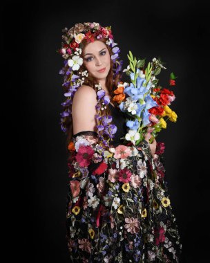 Celtic Bahar Tanrıçası Fantezi Kostümü Olarak Bir Kadın Modelinin Stüdyosu Gerçek Çiçekler ve başlıklı Beltane Pagan Mitolojisinden esinlenilerek izole edilmiş Karanlık Stüdyo Arkaplanı üzerine poz vermektedir.