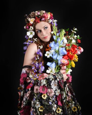 Celtic Bahar Tanrıçası Fantezi Kostümü Olarak Bir Kadın Modelinin Stüdyosu Gerçek Çiçekler ve başlıklı Beltane Pagan Mitolojisinden esinlenilerek izole edilmiş Karanlık Stüdyo Arkaplanı üzerine poz vermektedir.