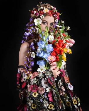 Celtic Bahar Tanrıçası Fantezi Kostümü Olarak Bir Kadın Modelinin Stüdyosu Gerçek Çiçekler ve başlıklı Beltane Pagan Mitolojisinden esinlenilerek izole edilmiş Karanlık Stüdyo Arkaplanı üzerine poz vermektedir.