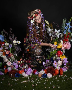 Celtic Bahar Tanrıçası Olarak Kadın Modellerinin Stüdyo Portreleri, Beltane Pagan Mitolojisinden esinlenilmiş Çiçek Peri Fantezi Kostümü. İzole edilmiş Karanlık Stüdyo Arkaplan 'da klasik oturma pozu