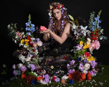 Celtic Bahar Tanrıçası Olarak Kadın Modellerinin Stüdyo Portreleri, Beltane Pagan Mitolojisinden esinlenilmiş Çiçek Peri Fantezi Kostümü. İzole edilmiş Karanlık Stüdyo Arkaplan 'da klasik oturma pozu