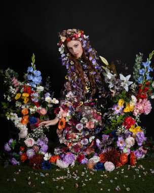 Celtic Bahar Tanrıçası Olarak Kadın Modellerinin Stüdyo Portreleri, Beltane Pagan Mitolojisinden esinlenilmiş Çiçek Peri Fantezi Kostümü. İzole edilmiş Karanlık Stüdyo Arkaplan 'da klasik oturma pozu