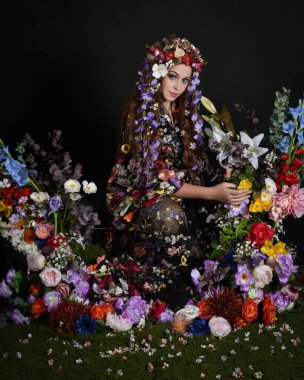 Celtic Bahar Tanrıçası Olarak Kadın Modellerinin Stüdyo Portreleri, Beltane Pagan Mitolojisinden esinlenilmiş Çiçek Peri Fantezi Kostümü. İzole edilmiş Karanlık Stüdyo Arkaplan 'da klasik oturma pozu