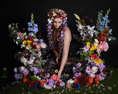 Celtic Bahar Tanrıçası Olarak Kadın Modellerinin Stüdyo Portreleri, Beltane Pagan Mitolojisinden esinlenilmiş Çiçek Peri Fantezi Kostümü. İzole edilmiş Karanlık Stüdyo Arkaplan 'da klasik oturma pozu