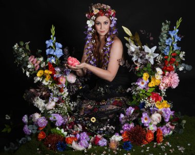 Celtic Bahar Tanrıçası Olarak Kadın Modellerinin Stüdyo Portreleri, Beltane Pagan Mitolojisinden esinlenilmiş Çiçek Peri Fantezi Kostümü. İzole edilmiş Karanlık Stüdyo Arkaplan 'da klasik oturma pozu