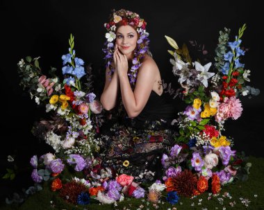 Celtic Bahar Tanrıçası Olarak Kadın Modellerinin Stüdyo Portreleri, Beltane Pagan Mitolojisinden esinlenilmiş Çiçek Peri Fantezi Kostümü. İzole edilmiş Karanlık Stüdyo Arkaplan 'da klasik oturma pozu