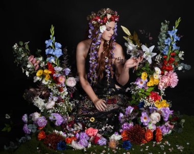 Celtic Bahar Tanrıçası Olarak Kadın Modellerinin Stüdyo Portreleri, Beltane Pagan Mitolojisinden esinlenilmiş Çiçek Peri Fantezi Kostümü. İzole edilmiş Karanlık Stüdyo Arkaplan 'da klasik oturma pozu