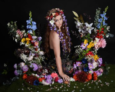 Celtic Bahar Tanrıçası Olarak Kadın Modellerinin Stüdyo Portreleri, Beltane Pagan Mitolojisinden esinlenilmiş Çiçek Peri Fantezi Kostümü. İzole edilmiş Karanlık Stüdyo Arkaplan 'da klasik oturma pozu