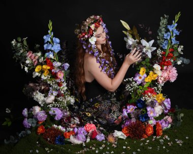 Celtic Bahar Tanrıçası Olarak Kadın Modellerinin Stüdyo Portreleri, Beltane Pagan Mitolojisinden esinlenilmiş Çiçek Peri Fantezi Kostümü. İzole edilmiş Karanlık Stüdyo Arkaplan 'da klasik oturma pozu