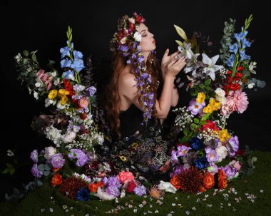 Celtic Bahar Tanrıçası Olarak Kadın Modellerinin Stüdyo Portreleri, Beltane Pagan Mitolojisinden esinlenilmiş Çiçek Peri Fantezi Kostümü. İzole edilmiş Karanlık Stüdyo Arkaplan 'da klasik oturma pozu