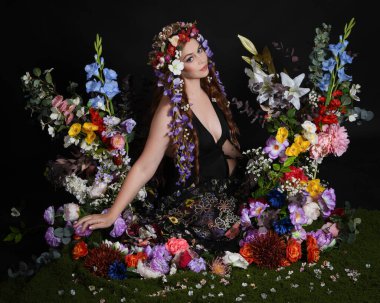 Celtic Bahar Tanrıçası Olarak Kadın Modellerinin Stüdyo Portreleri, Beltane Pagan Mitolojisinden esinlenilmiş Çiçek Peri Fantezi Kostümü. İzole edilmiş Karanlık Stüdyo Arkaplan 'da klasik oturma pozu