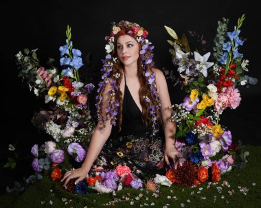 Celtic Bahar Tanrıçası Olarak Kadın Modellerinin Stüdyo Portreleri, Beltane Pagan Mitolojisinden esinlenilmiş Çiçek Peri Fantezi Kostümü. İzole edilmiş Karanlık Stüdyo Arkaplan 'da klasik oturma pozu