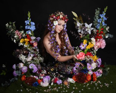 Celtic Bahar Tanrıçası Olarak Kadın Modellerinin Stüdyo Portreleri, Beltane Pagan Mitolojisinden esinlenilmiş Çiçek Peri Fantezi Kostümü. İzole edilmiş Karanlık Stüdyo Arkaplan 'da klasik oturma pozu