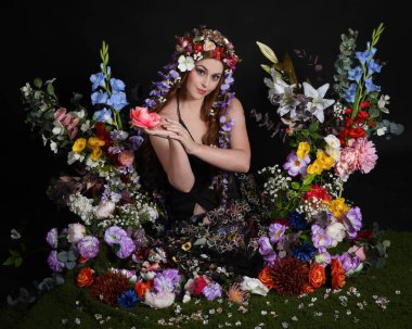 Celtic Bahar Tanrıçası Olarak Kadın Modellerinin Stüdyo Portreleri, Beltane Pagan Mitolojisinden esinlenilmiş Çiçek Peri Fantezi Kostümü. İzole edilmiş Karanlık Stüdyo Arkaplan 'da klasik oturma pozu