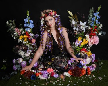 Celtic Bahar Tanrıçası Olarak Kadın Modellerinin Stüdyo Portreleri, Beltane Pagan Mitolojisinden esinlenilmiş Çiçek Peri Fantezi Kostümü. İzole edilmiş Karanlık Stüdyo Arkaplan 'da klasik oturma pozu