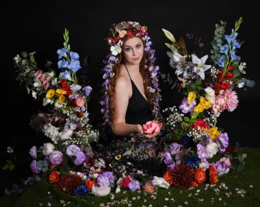 Celtic Bahar Tanrıçası Olarak Kadın Modellerinin Stüdyo Portreleri, Beltane Pagan Mitolojisinden esinlenilmiş Çiçek Peri Fantezi Kostümü. İzole edilmiş Karanlık Stüdyo Arkaplan 'da klasik oturma pozu