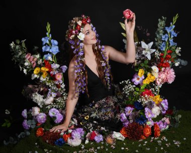 Celtic Bahar Tanrıçası Olarak Kadın Modellerinin Stüdyo Portreleri, Beltane Pagan Mitolojisinden esinlenilmiş Çiçek Peri Fantezi Kostümü. İzole edilmiş Karanlık Stüdyo Arkaplan 'da klasik oturma pozu