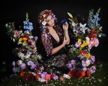 Celtic Bahar Tanrıçası Olarak Kadın Modellerinin Stüdyo Portreleri, Beltane Pagan Mitolojisinden esinlenilmiş Çiçek Peri Fantezi Kostümü. İzole edilmiş Karanlık Stüdyo Arkaplan 'da klasik oturma pozu