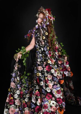 Celtic Bahar Tanrıçası Olarak Kadın Model Stüdyo Portreleri, Beltane Pagan Mitolojisinden esinlenerek Çiçek Fantezi Pelerini Kostümü. Kol hareketleriyle klasik poz, izole edilmiş Karanlık Arkaplan