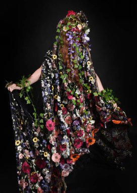 Celtic Bahar Tanrıçası Olarak Kadın Model Stüdyo Portreleri, Beltane Pagan Mitolojisinden esinlenerek Çiçek Fantezi Pelerini Kostümü. Kol hareketleriyle klasik poz, izole edilmiş Karanlık Arkaplan