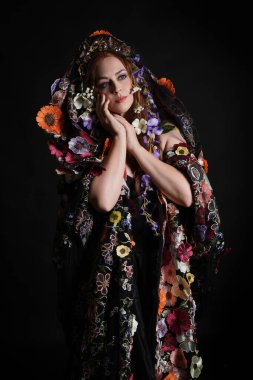 Celtic Bahar Tanrıçası Olarak Kadın Model Stüdyo Portreleri, Beltane Pagan Mitolojisinden esinlenerek Çiçek Fantezi Pelerini Kostümü. Kol hareketleriyle klasik poz, izole edilmiş Karanlık Arkaplan