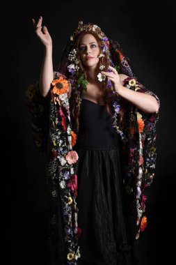 Celtic Bahar Tanrıçası Olarak Kadın Model Stüdyo Portreleri, Beltane Pagan Mitolojisinden esinlenerek Çiçek Fantezi Pelerini Kostümü. Kol hareketleriyle klasik poz, izole edilmiş Karanlık Arkaplan