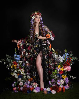 Celtic Bahar Tanrıçası Olarak Kadın Modellerinin Stüdyo Portreleri, Beltane Pagan Mitolojisinden esinlenilmiş Çiçek Peri Fantezi Kostümü. İzole edilmiş Karanlık Stüdyo Arkaplanda Pelerinli Klasik Duruş