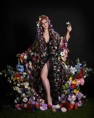 Celtic Bahar Tanrıçası Olarak Kadın Modellerinin Stüdyo Portreleri, Beltane Pagan Mitolojisinden esinlenilmiş Çiçek Peri Fantezi Kostümü. İzole edilmiş Karanlık Stüdyo Arkaplanda Pelerinli Klasik Duruş