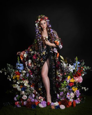 Celtic Bahar Tanrıçası Olarak Kadın Modellerinin Stüdyo Portreleri, Beltane Pagan Mitolojisinden esinlenilmiş Çiçek Peri Fantezi Kostümü. İzole edilmiş Karanlık Stüdyo Arkaplanda Pelerinli Klasik Duruş