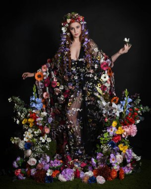 Celtic Bahar Tanrıçası Olarak Kadın Modellerinin Stüdyo Portreleri, Beltane Pagan Mitolojisinden esinlenilmiş Çiçek Peri Fantezi Kostümü. İzole edilmiş Karanlık Stüdyo Arkaplanda Pelerinli Klasik Duruş