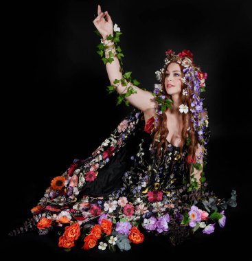 Celtic Bahar Tanrıçası Olarak Kadın Model Stüdyo Portreleri, Beltane Pagan Mitolojisinden esinlenerek Çiçek Fantezi Pelerini Kostümü. Klasik oturma pozisyonu, kollar uzanıyor. izole edilmiş Karanlık Arkaplan