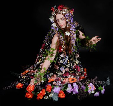 Celtic Bahar Tanrıçası Olarak Kadın Model Stüdyo Portreleri, Beltane Pagan Mitolojisinden esinlenerek Çiçek Fantezi Pelerini Kostümü. Klasik oturma pozisyonu, kollar uzanıyor. izole edilmiş Karanlık Arkaplan