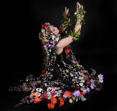 Celtic Bahar Tanrıçası Olarak Kadın Model Stüdyo Portreleri, Beltane Pagan Mitolojisinden esinlenerek Çiçek Fantezi Pelerini Kostümü. Klasik oturma pozisyonu, kollar uzanıyor. izole edilmiş Karanlık Arkaplan