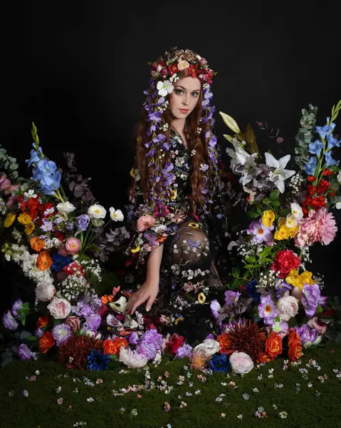 Celtic Bahar Tanrıçası Olarak Kadın Modellerinin Stüdyo Portreleri, Beltane Pagan Mitolojisinden esinlenilmiş Çiçek Peri Fantezi Kostümü. İzole edilmiş Karanlık Stüdyo Arkaplan 'da klasik oturma pozu