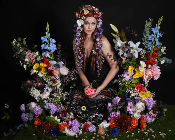 Celtic Bahar Tanrıçası Olarak Kadın Modellerinin Stüdyo Portreleri, Beltane Pagan Mitolojisinden esinlenilmiş Çiçek Peri Fantezi Kostümü. İzole edilmiş Karanlık Stüdyo Arkaplan 'da klasik oturma pozu