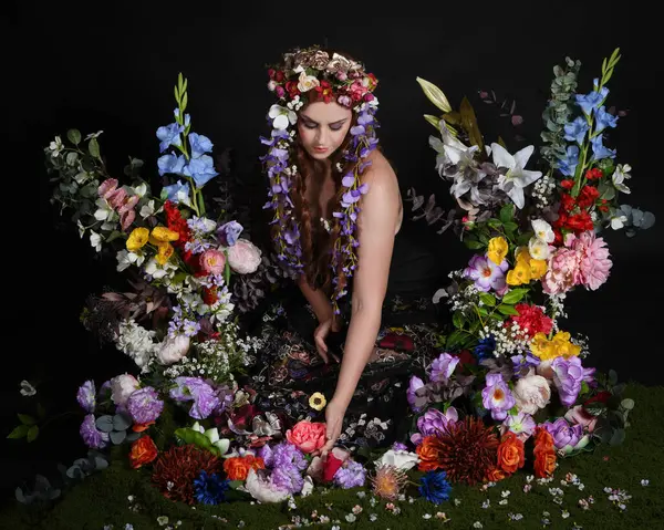 Celtic Bahar Tanrıçası Olarak Kadın Modellerinin Stüdyo Portreleri, Beltane Pagan Mitolojisinden esinlenilmiş Çiçek Peri Fantezi Kostümü. İzole edilmiş Karanlık Stüdyo Arkaplan 'da klasik oturma pozu